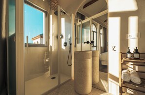 Un baño moderno con cabina de ducha de vidrio, un jarrón beige grande y un perchero con toallas.