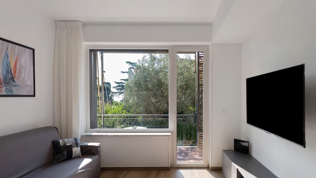Un soggiorno moderno con un divano, una televisione a schermo piatto e un'ampia finestra vista sul verde.