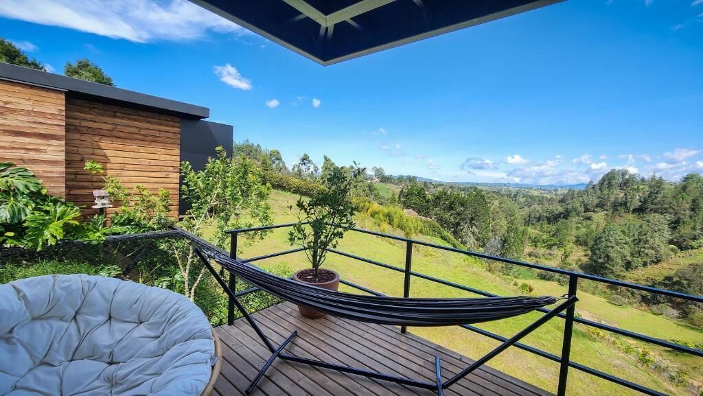 A wooden deck with a hammock and a cushioned chair, overlooking a lush green landscape.