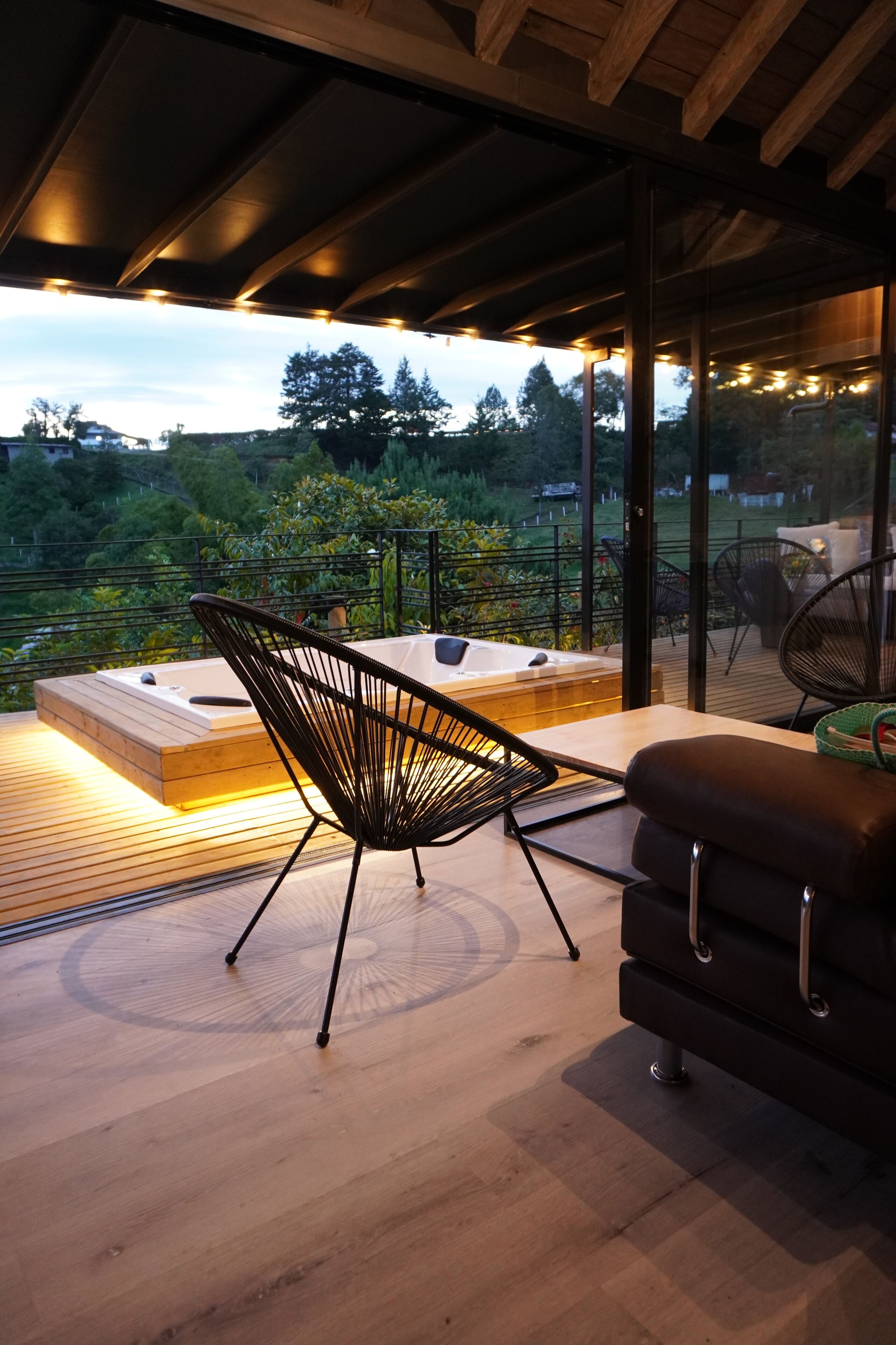 Een modern buitenzitgedeelte met een houten terras, een zwarte stoel, een bank en een jacuzzi.