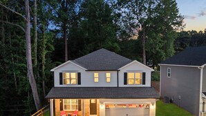 Une maison à deux étages avec un garage, une véranda couverte avec des chaises rouges et une pelouse bien entretenue.