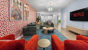 Un salon comprenant un canapé, des fauteuils, une table basse et un téléviseur affichant le logo « NETFLIX ».