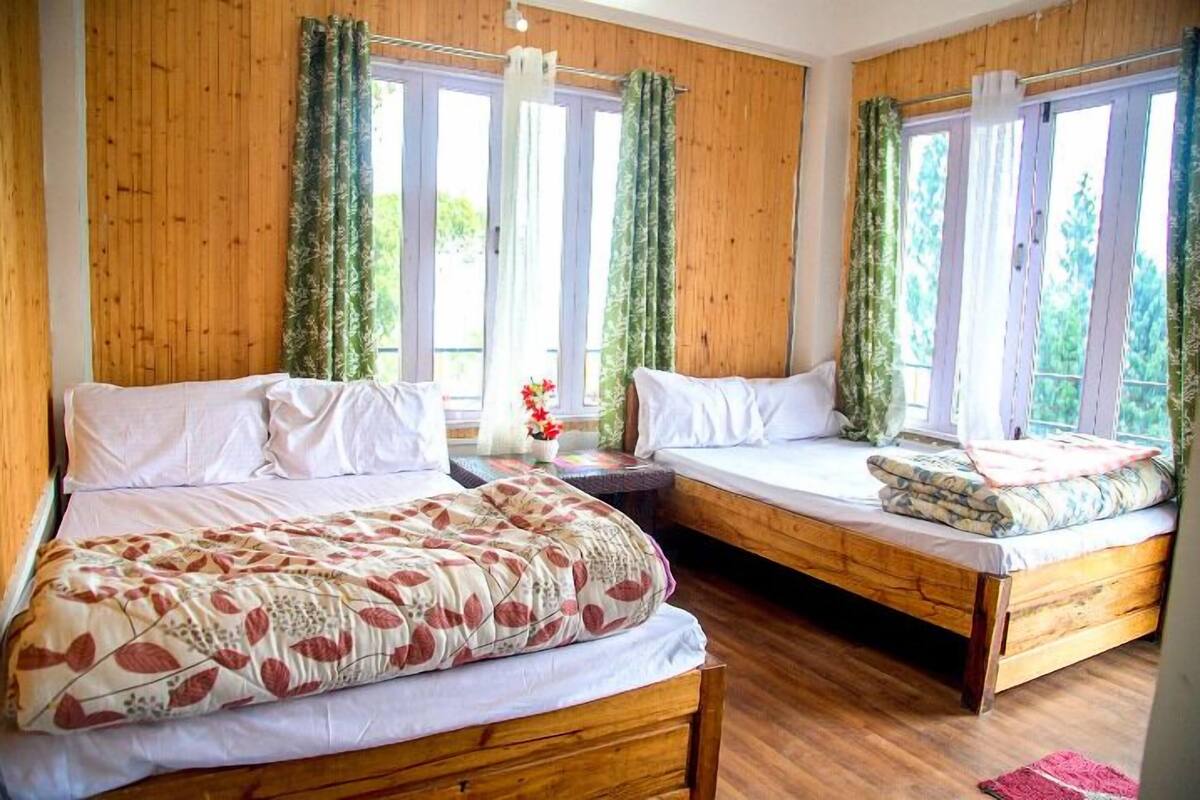 A room with two wooden beds, large windows with curtains, and a wooden floor.