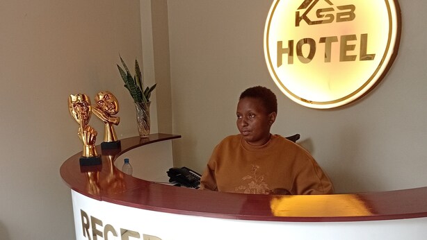 A reception desk with a sign reading "RECEPTION" and a circular sign above it that says "KGB HOTEL". - KSB HOTEL (Mwanza)