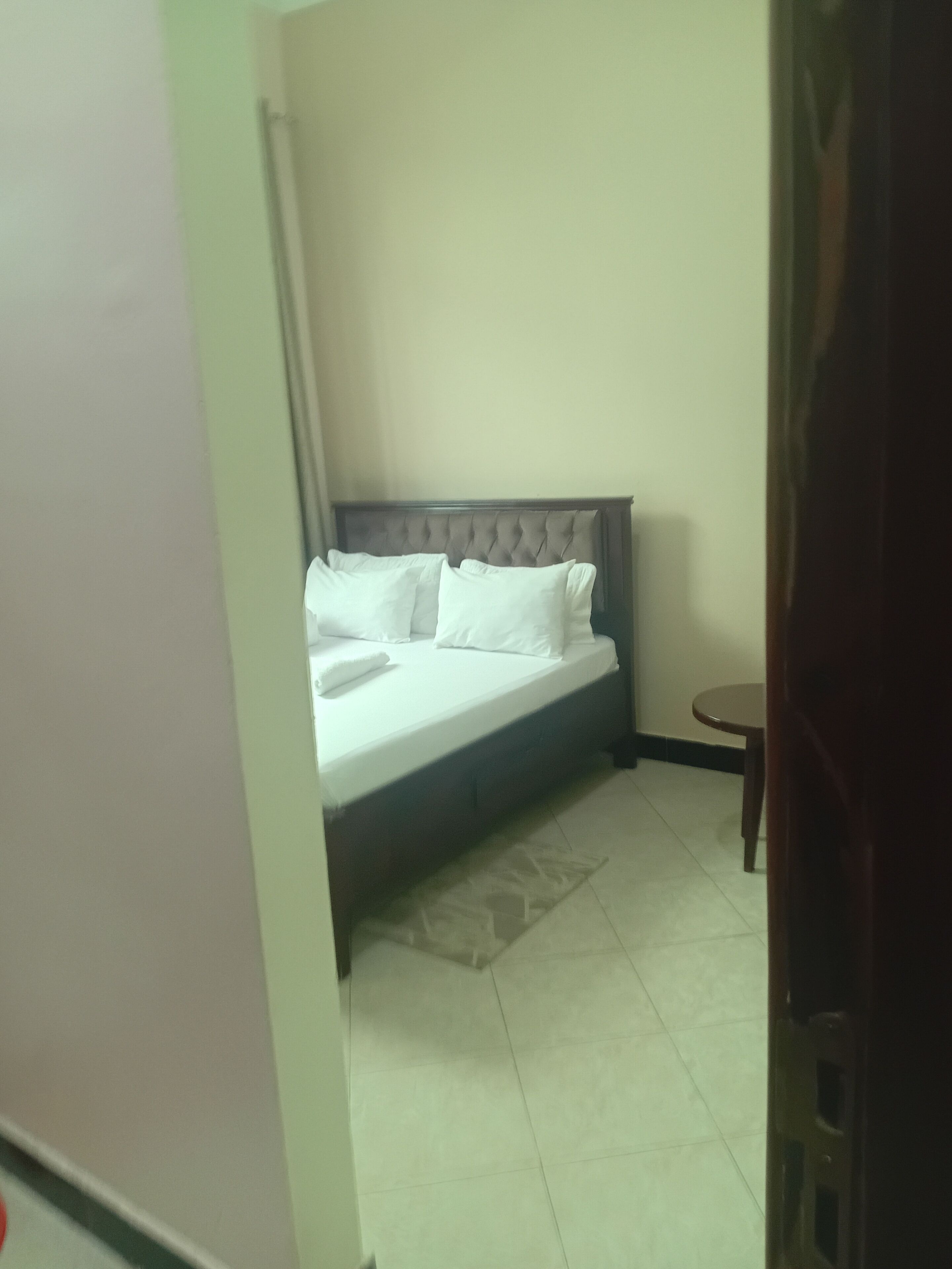 Un dormitorio con una cama, una mesita redonda y una pared lisa.