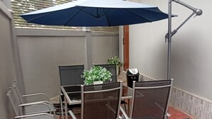 A patio area with a table and chairs, a potted plant, and a blue umbrella. - KSB HOTEL (Mwanza)