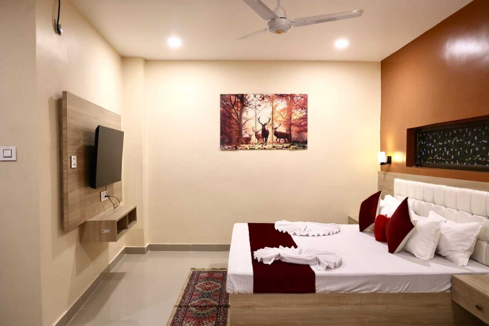Un dormitorio moderno con una cama grande, una televisión montada, un ventilador de techo y una obra de arte en la pared.