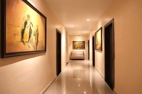 A hallway with artwork on the walls, a bench, and doors leading to rooms. - Regal Guest House by ROH (Nagaon)