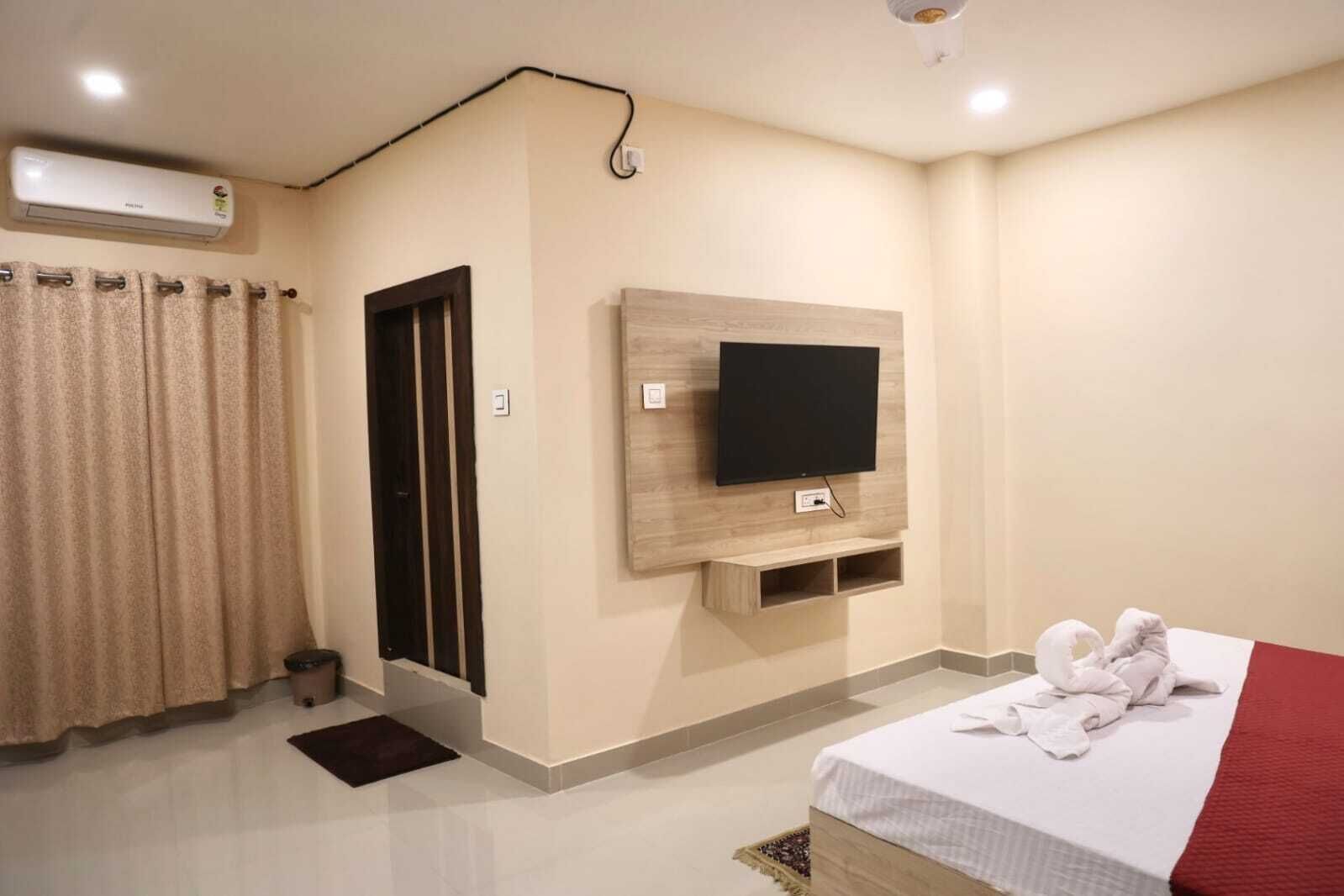 A hotel room with a bed, a TV mounted on the wall, a door, and a curtain.