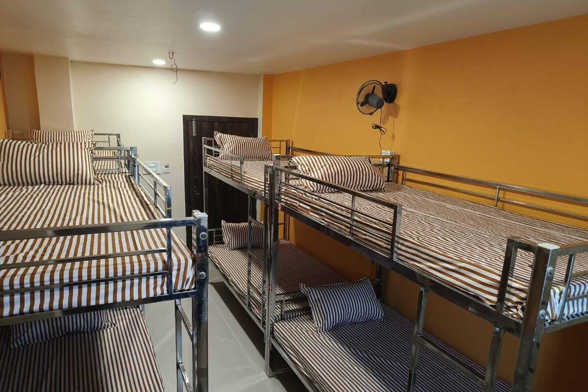 A dormitory room with bunk beds, a fan, and a door.