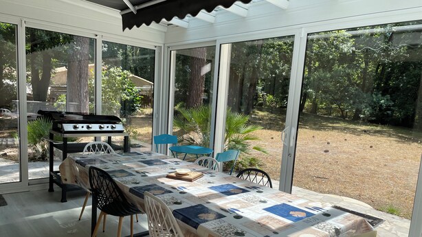 A conservatory with a dining table, chairs, and a barbecue grill. - Villa with air-conditioned areas, close to the sea, the forest, the village, and the harbor. (La Tremblade)
