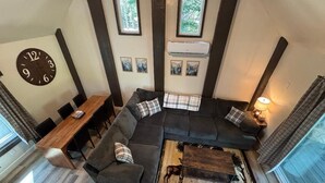 En moderne stue med en modulsofa, et træsofabord og et spiseområde med et træbord og stole. Et stort vægur og indrammede kunstværker hænger over sofaen.
