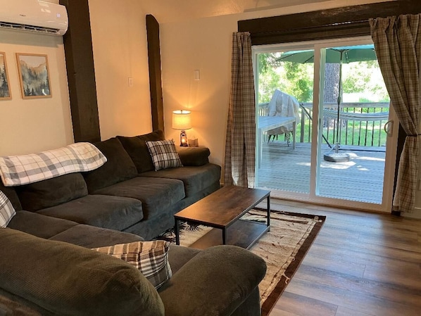 A cozy living room with a sofa, a coffee table, and a lamp. There is a sliding glass door leading to an outdoor deck.