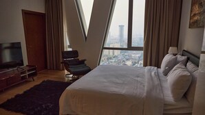 A bedroom with a large bed, a TV, a chair, and a view of a cityscape through a window. - Altair Luxury Colombo by Miracle apartment,fitness room in enchanting Colombo (Colombo)