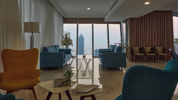 A modern living room with a view of a city skyline, featuring blue sofas, a coffee table, and a lamp. - Altair Luxury Colombo by Miracle apartment,fitness room in enchanting Colombo (Colombo)