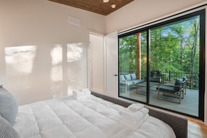 Un dormitorio con una cama grande, una puerta corrediza de vidrio que da a una terraza exterior con asientos.