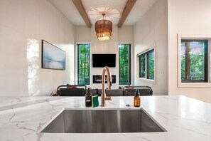A modern kitchen with a large marble countertop, a copper faucet, and a built-in TV above the sink.