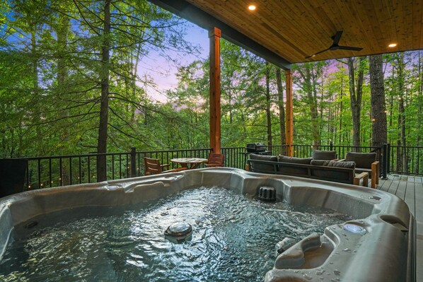 A hot tub on a wooden deck with a view of a forest.
