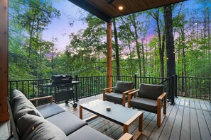 Terraza con mobiliario exterior, una parrilla y vistas a un bosque.