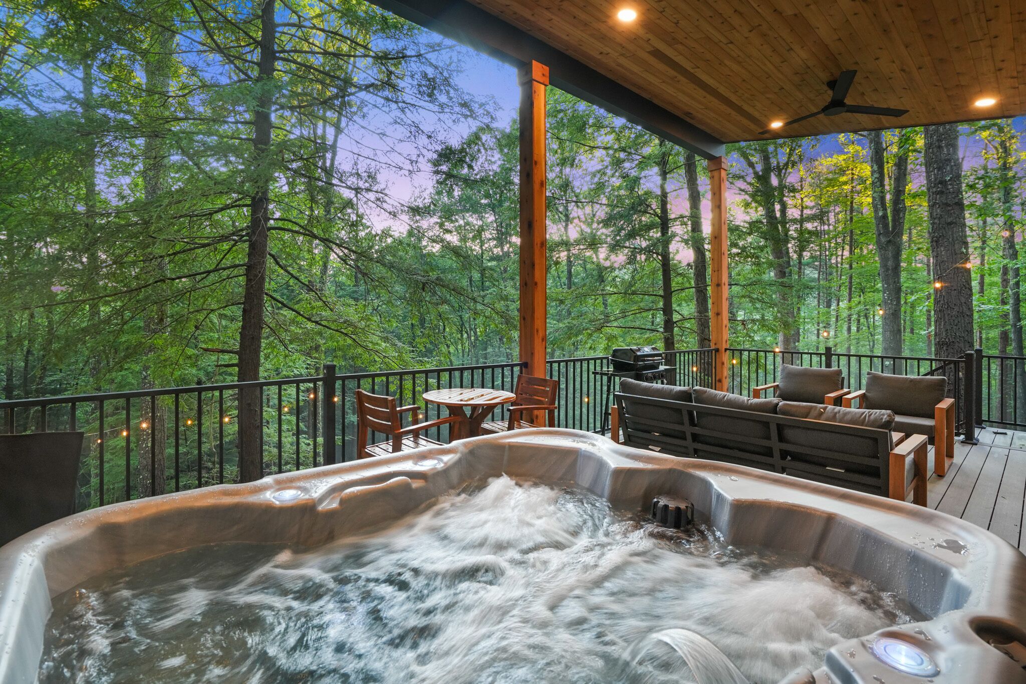 A hot tub on a wooden deck with a view of a forest.