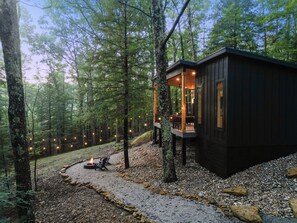 Eine Holzhütte mit einer Terrasse, umgeben von Bäumen und einem Kiesweg.