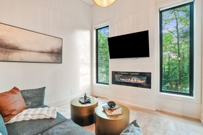 Moderni olohuone, jossa on takka, suuret ikkunat ja litteänäyttöinen televisio.