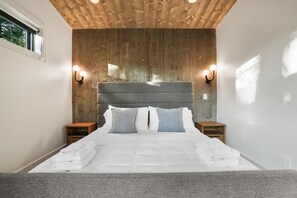 Un dormitorio moderno con techo de madera, una cama grande con ropa de cama blanca, dos mesitas de noche e iluminación empotrada.