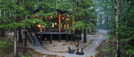 A cabin surrounded by trees with a deck and outdoor seating area.