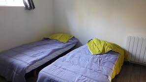Two single beds with purple bedding and yellow pillows in a room with white walls and a radiator.