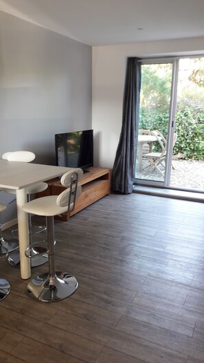 A modern living room with a dining area, a TV, and a sliding glass door leading to an outdoor patio.