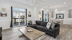 A spacious living room with a dark grey sofa, a wooden coffee table, and a dining area with a white table and chairs. - Sea Turtle Shanty, Navarre Beach (Navarre)