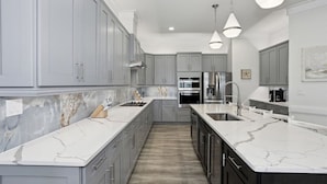 A modern kitchen with grey cabinets, a marble countertop, stainless steel appliances, and pendant lighting. - Sea Turtle Shanty, Navarre Beach (Navarre)