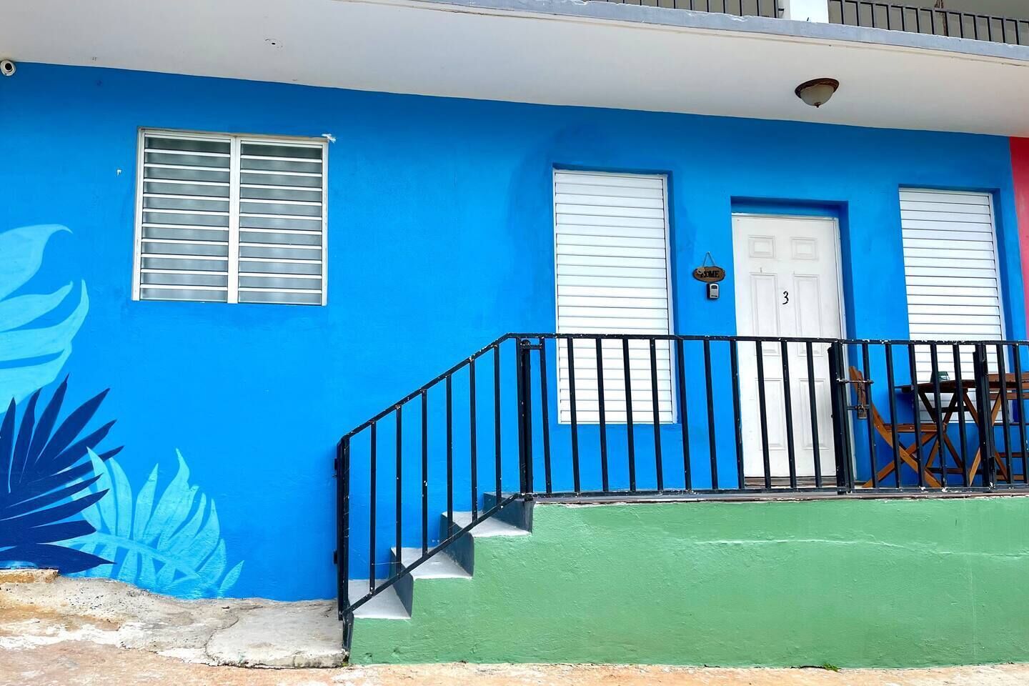 A building with a blue exterior, a white door, and a black railing.