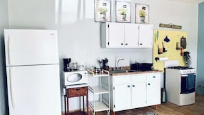 A compact kitchen with white cabinets, a microwave, a stove, and a small dining area with a chair. - Nature Escape Solar Energy Close to Port (Ceiba)