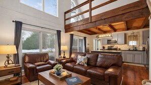 A spacious living room with leather sofas, a wooden coffee table, and a view of the kitchen.