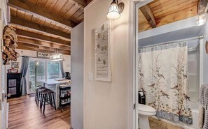 Ein rustikales Interieur mit Holzbalken, einer Küchenzeile mit Hockern, einer weißen Toilette und einer Dusche mit floralem Vorhang.