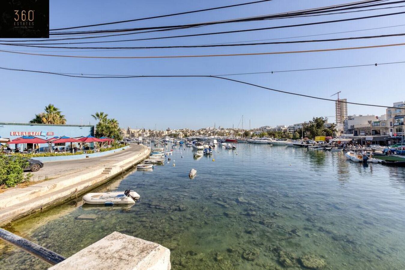 Un puerto deportivo con barcos amarrados, un frente marítimo despejado y edificios al fondo.
