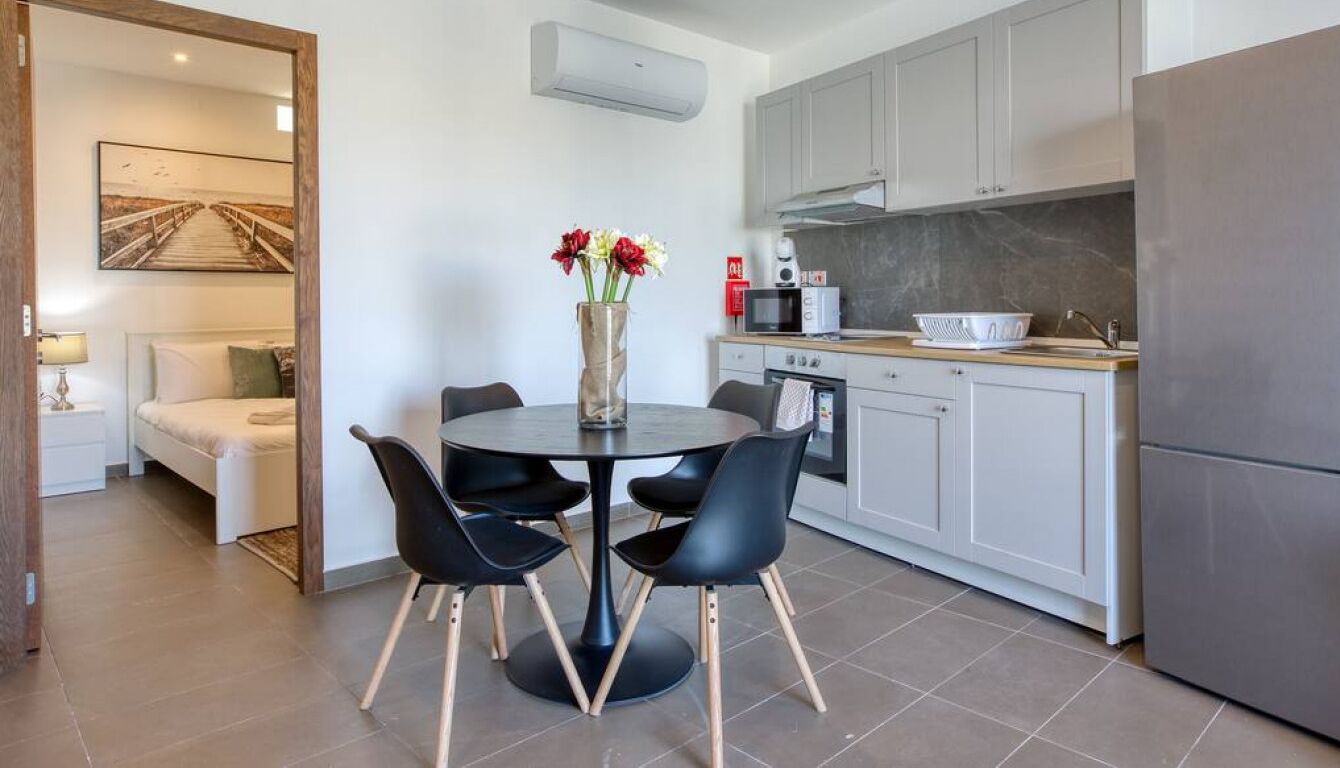 A modern kitchen with grey cabinets, a stainless steel refrigerator, and a dining area with a round table and black chairs.
