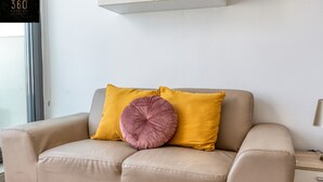 A beige leather sofa with two cushions, one yellow and one pink, against a white wall with a cabinet above.