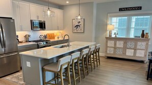 Una cocina moderna con armarios blancos, electrodomésticos de acero inoxidable y una isla central con taburetes de bar.