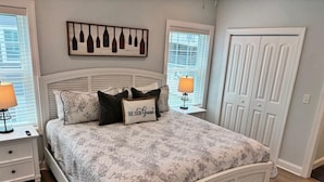 Un dormitorio ordenado con cama, dos mesitas de noche, un cuadro en la pared y una puerta.