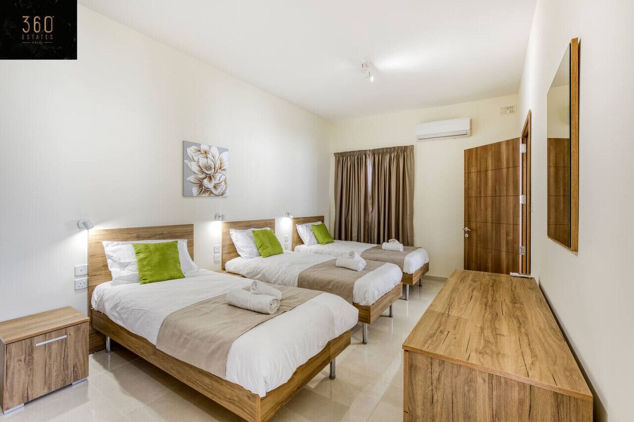 Een hotelkamer met drie houten bedden, een houten bureau, een spiegel en een wandairconditioner.