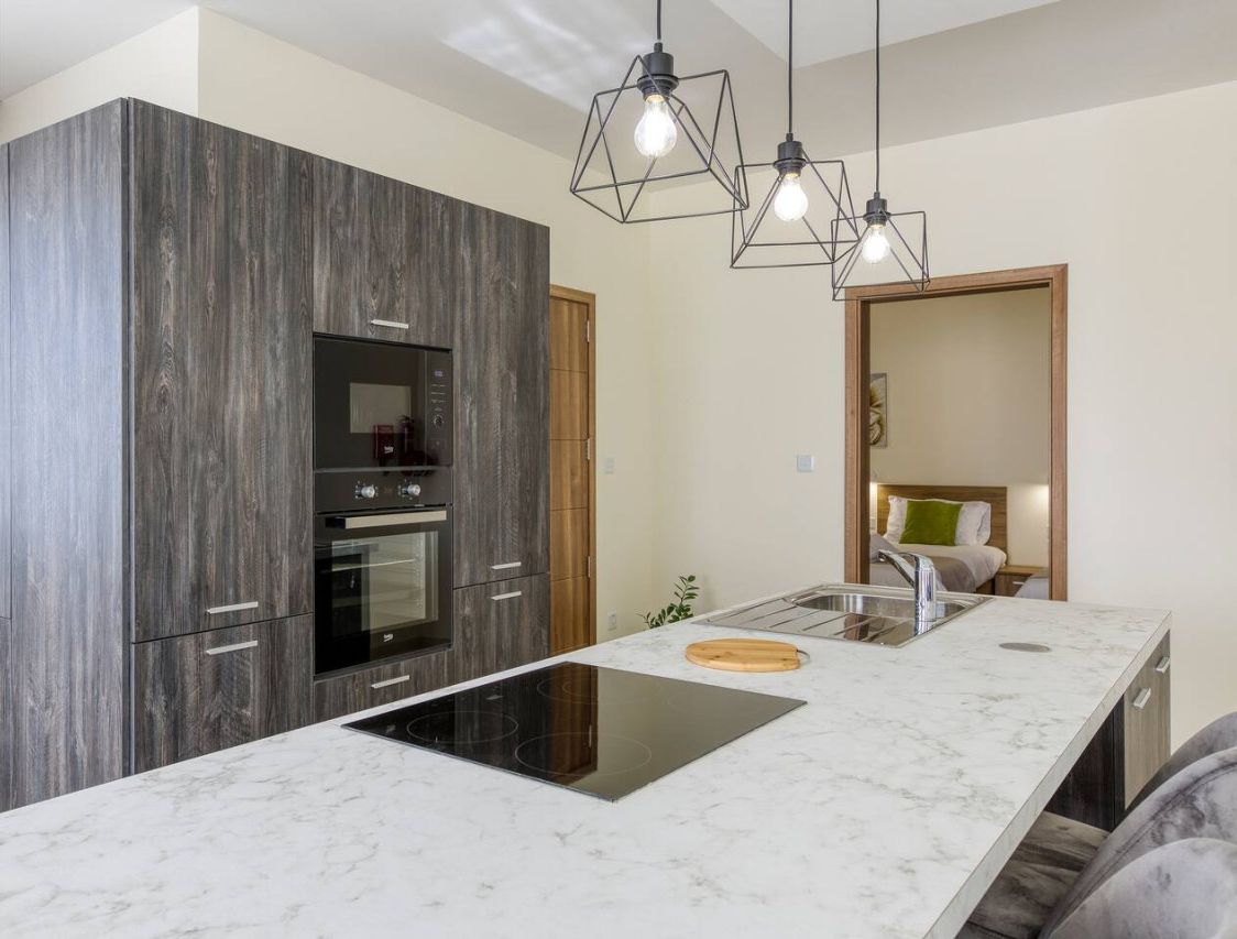 A modern kitchen with a large island, built-in oven, and pendant lighting.