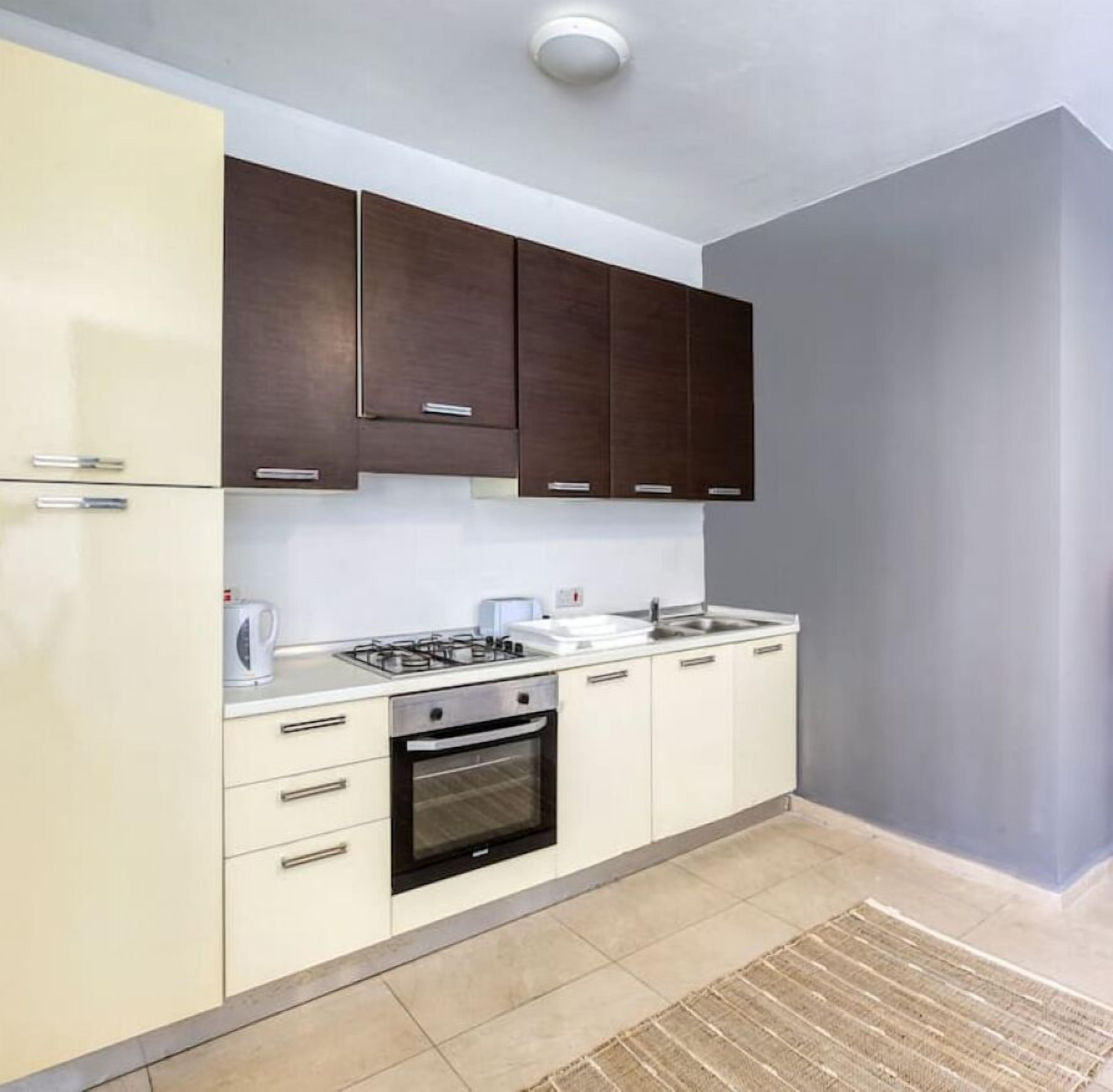 Una cucina compatta con fornelli, forno e lavello, caratterizzata da mobili chiari e un piano di lavoro scuro.