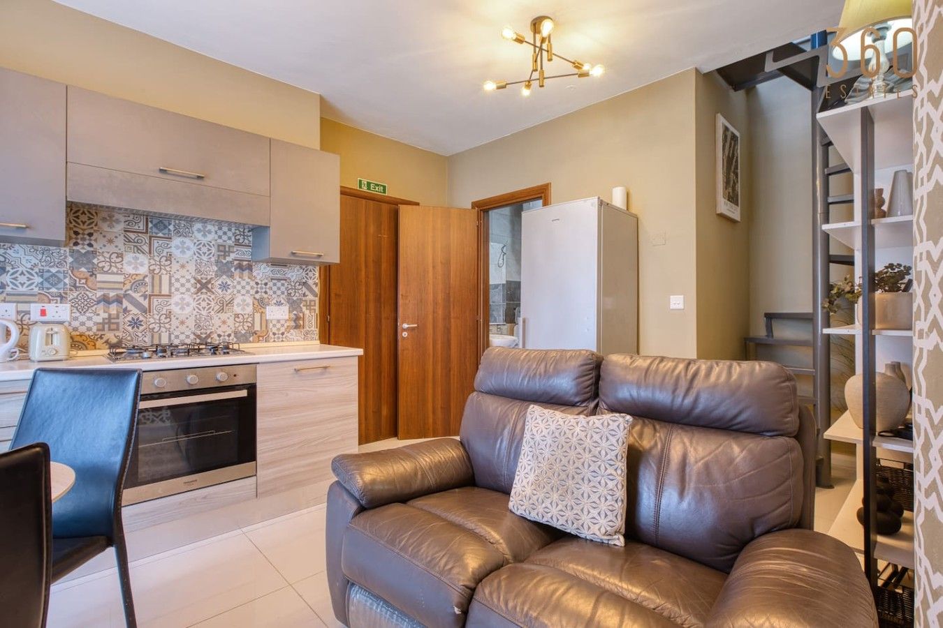 Una cucina moderna con forno integrato, una zona pranzo con una sedia e un divano in pelle con un cuscino decorativo.