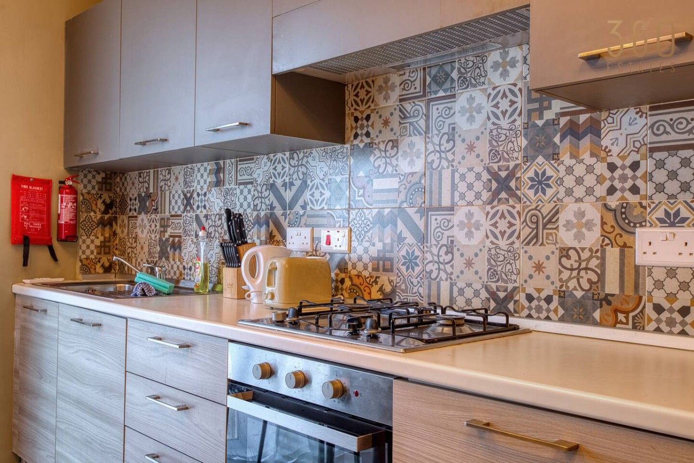 Una cucina con piastrelle decorate, un fornello a gas, un tostapane e un estintore.