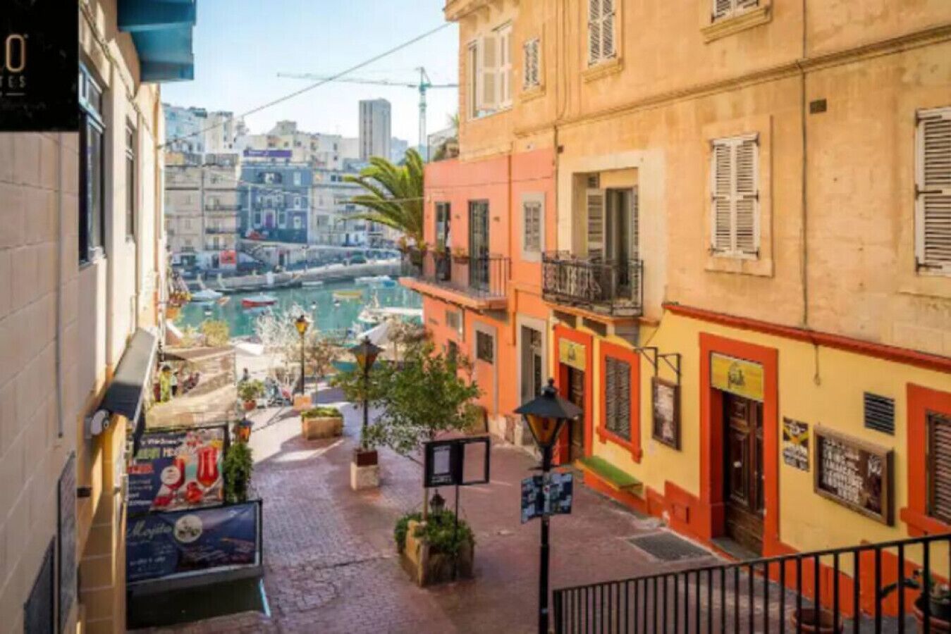 Une rue étroite, bordée de bâtiments des deux côtés, offrant une vue dégagée sur l’eau, et quelques lampadaires.