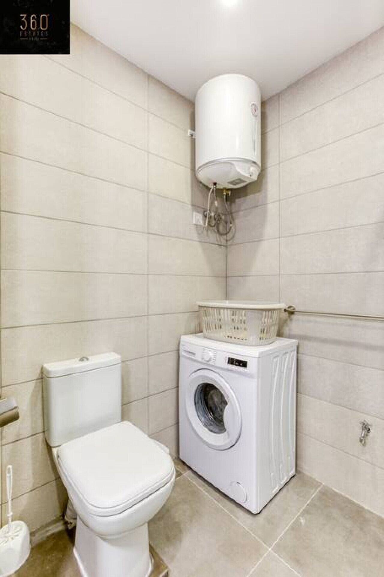 Une petite salle de bain propre, équipée de toilettes, d’un lave-linge et d’un chauffe-eau.