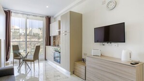 A modern living room with a glass dining table, a sofa, and a TV mounted on the wall. - Cozy 1BR home in the centre of St Julians w/WIFI (San Ġiljan)
