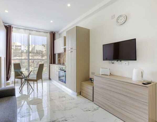 A modern living room with a glass dining table, a sofa, and a TV mounted on the wall.